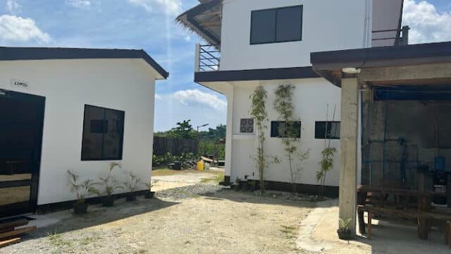 Two modern white buildings with black trim in Siargao, set around a gravel courtyard under a bright, partly cloudy sky.