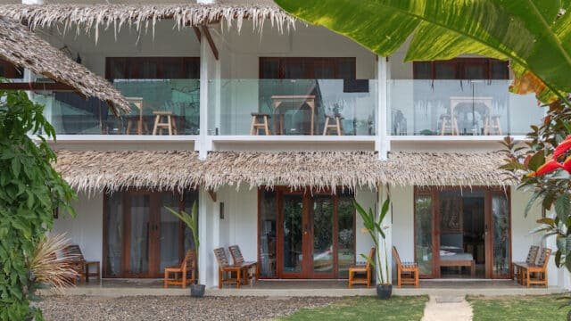 Two-story tropical Siargao building with thatched roof, balconies, and wooden chairs, surrounded by lush greenery.