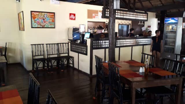 Cozy Siargao restaurant interior with wooden tables, chairs, counter; wall art and Illy sign are visible.