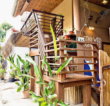 Wooden outdoor staircase with potted plants and a Stay Wild Ocean Child sign, evoking the laid-back vibes of Siargao.