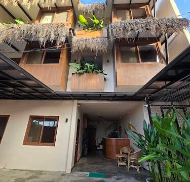 Three-story Siargao building with wooden accents, thatched roofing, and potted plants on balconies and in the entryway.