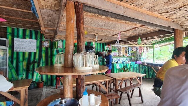 Open-air eatery in Siargao with wooden tables, bamboo decor, and people seated inside under a thatched roof.