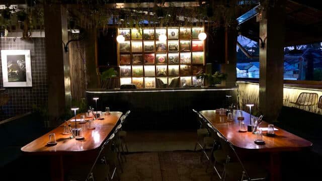Dimly lit Siargao restaurant with two wooden tables, chairs, and a backlit wall adorned with album covers.
