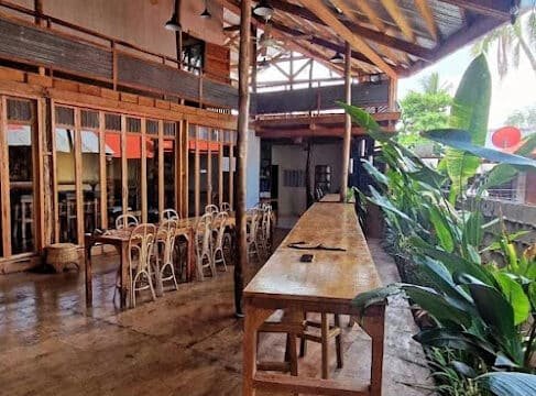 Open-air café in Siargao with wooden tables, stools, and chairs, surrounded by green plants and rustic decor.
