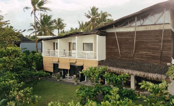 Two-story tropical Siargao building with balconies, surrounded by lush greenery and palm trees under a cloudy sky.