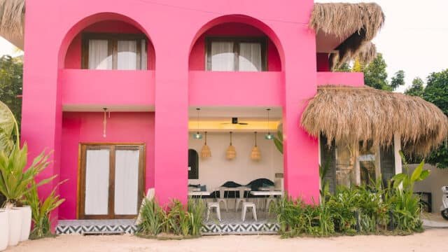 A bright pink building in Siargao with arched windows, thatched awnings, and lush green plants out front.