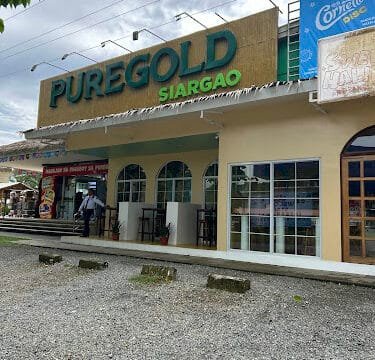 Puregold Siargao storefront with large green signage, tables, and a few people enjoying a cloudy day on Siargao.