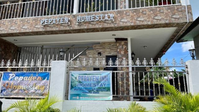 Two signs for Pepayen Homestay hang on a stone building’s fence in Siargao, with plants in front and balconies above.