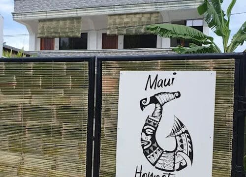 A sign reading Maui Homestay with a phone number is on a bamboo gate, evoking Siargao vibes in front of a modern building.