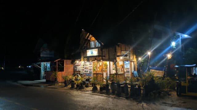 A small, rustic shop in Siargao with bright lights and potted plants outside, illuminated at night on a quiet street.