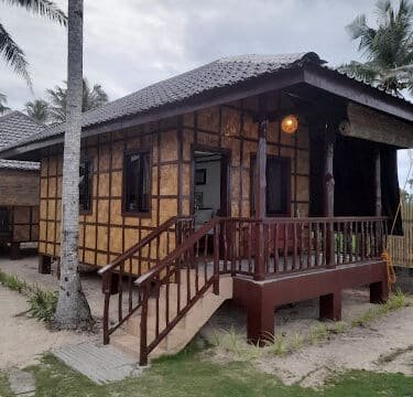 A small bamboo house with a front porch, surrounded by palm trees and cloudy Siargao skies.