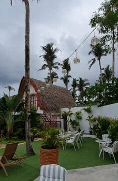 Outdoor patio with tables and chairs, palm trees, lush greenery, and a thatched-roof building evoking Siargao’s tropical charm.