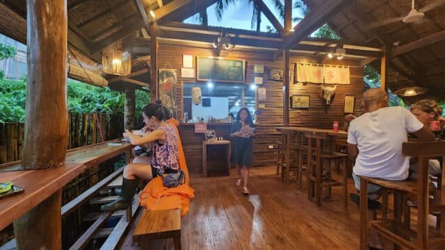 People dining in a cozy, rustic wooden restaurant in Siargao with an open-air tropical view and warm lighting.