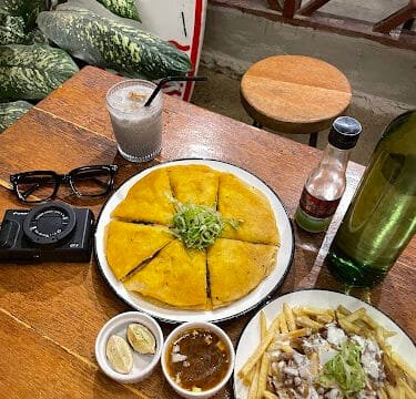 A table in Siargao with a quesadilla, loaded fries, sauces, a drink, sunglasses, and a camera.