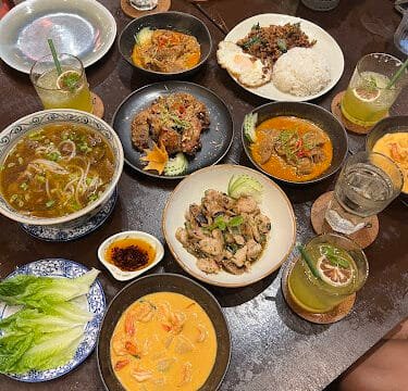 A table filled with various Thai dishes, drinks, rice, curry, soup, and plates of vegetables in a cozy Siargao setting.
