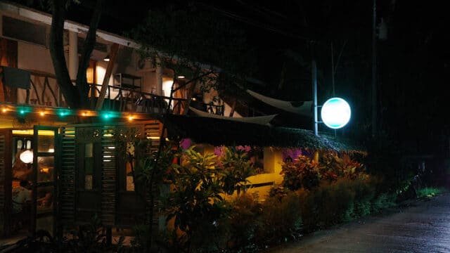 A cozy Siargao restaurant with warm lights and greenery, beautifully viewed from the street at night.