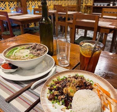 A table in Siargao with ramen, rice dish, iced tea, a beer bottle, and condiments at an outdoor restaurant.