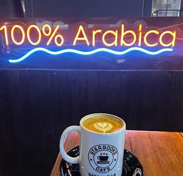 A cup of coffee on a table in Siargao glows beneath a neon sign that reads 100% Arabica.