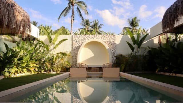 A serene pool with lounge chairs, surrounded by lush plants and palm trees under Siargao’s clear blue sky.