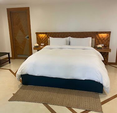 A neatly made bed with white linens in a clean, modern Siargao bedroom featuring beige walls and wood accents.