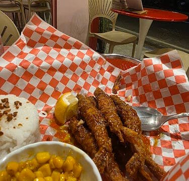 Fried shrimp with a lemon wedge, white rice, and corn on a red checkered tray in a casual Siargao restaurant.