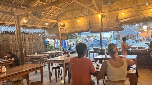 People seated at wooden tables in a Siargao open-air restaurant with a thatched roof, street views just outside.