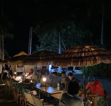 People sitting under straw umbrellas at a Siargao night market, illuminated by warm lights.