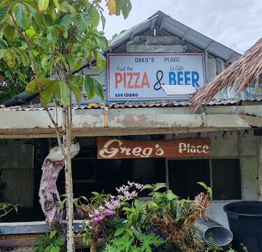 A rustic Siargao restaurant with signs reading Gregs Place and Pizza & Beer, nestled amid lush greenery.