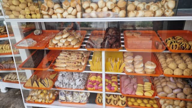 A bakery display case in Siargao filled with various types of bread and colorful pastries on orange trays.