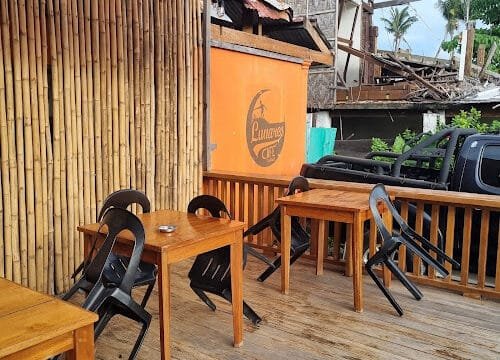 Wooden tables and black chairs on an outdoor patio with bamboo walls in Siargao, marked by an orange Lunares Cafe sign.