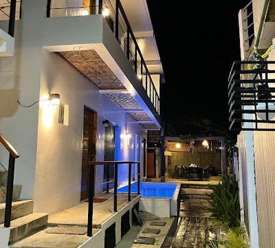 Modern two-story Siargao building at night with illuminated hallways and a small pool beside a walkway.