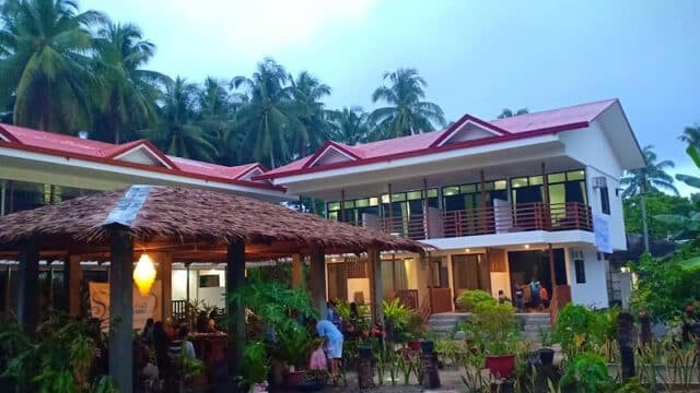 A tropical Siargao guesthouse with red roofs, surrounded by palm trees and lush greenery at dusk.