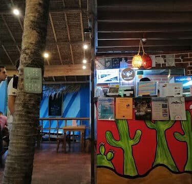 Indoor beach café in Siargao with colorful cactus mural, hanging lights, and a ‘Life is better at the beach’ sign on a tree.