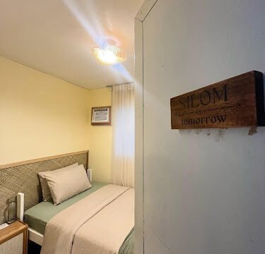 A cozy bedroom with a bed, soft lighting, and a door sign that reads SILOM tomorrow, bringing Siargao vibes to your stay.
