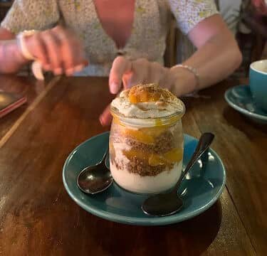 A layered dessert in a jar with two spoons on a blue plate; a woman sits in the background, evoking relaxed Siargao vibes.