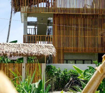 Modern Siargao tropical house with wooden slats, thatched roof, and lush green plants in the foreground.