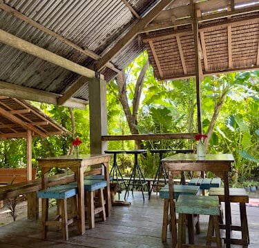 Open-air café with wooden tables and stools in Siargao, surrounded by lush green plants and natural light.