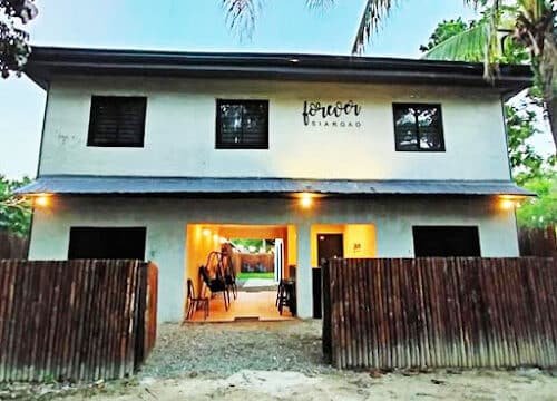 Two-story building with SIARGAO sign, wooden fence, open entrance, and palm trees surrounding this Siargao gem.