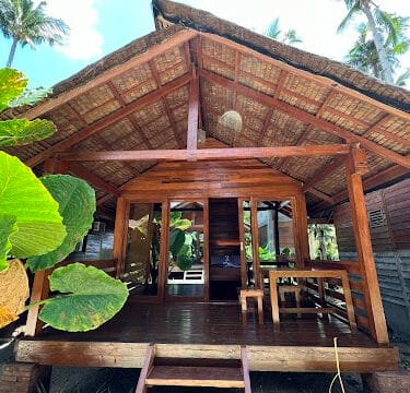 A wooden tropical hut with a thatched roof, open porch, and lush green plants—perfect for a relaxing Siargao retreat.