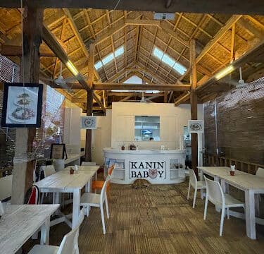 Rustic restaurant interior with wooden beams, white tables and chairs, and a KANIN BABOY sign at the counter in Siargao.