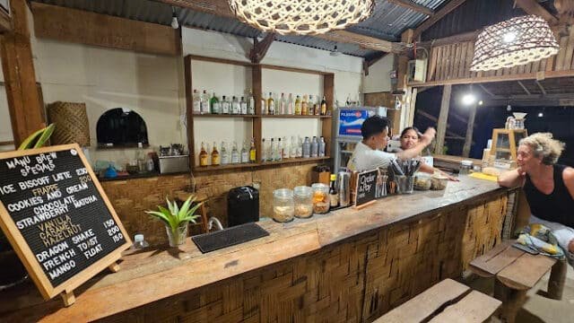 A cozy bamboo bar in Siargao with drinks, snacks, and two men talking across the counter at night.