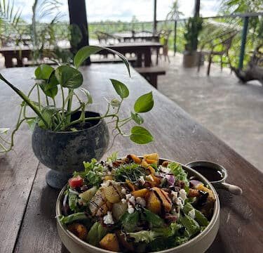A bowl of fresh salad and a potted plant on a wooden table in an open-air Siargao tropical café.