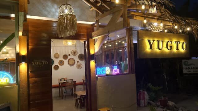 A cozy restaurant entrance at night in Siargao, warmly lit with a glowing YUGTO sign and hanging lights.