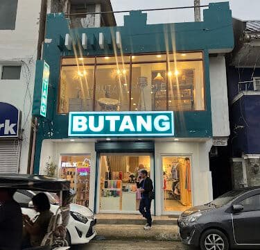 A two-story shop with a bright BUTANG sign, glass windows, and people walking past on the lively streets of Siargao.