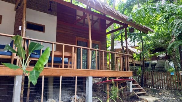 Wooden bungalow with a porch and blue chairs, surrounded by lush tropical plants and trees in beautiful Siargao.