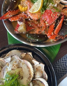 A Siargao seafood boil with crab, corn, and lemon slices sits beside cheesy baked scallops topped with green onions.