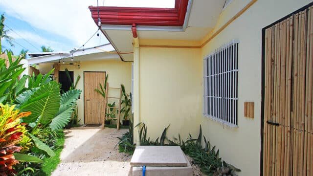 Charming small courtyard in Siargao with yellow walls, red roof, green plants, bamboo doors, and a barred window.