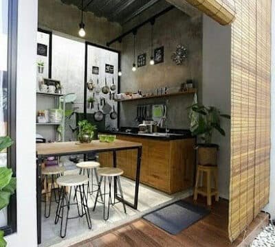 Modern small kitchen with wooden cabinets, bar stools, hanging lights, plants, and a Siargao-inspired bamboo blind at the entrance.