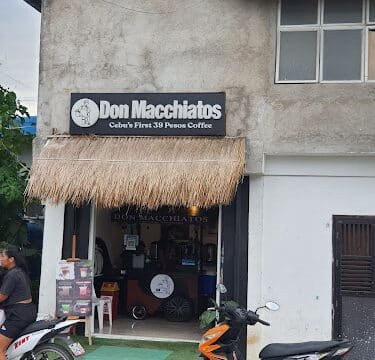 Street view of Don Macchiatos café in Siargao, with two parked motorbikes in front and a thatched roof entrance.