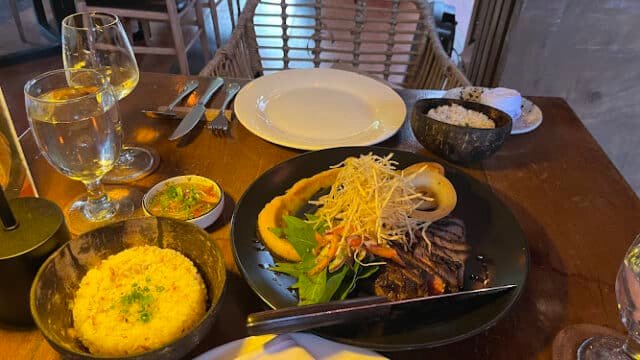 A dinner table with grilled steak, rice, vegetables, and sauces set in a cozy Siargao restaurant atmosphere.